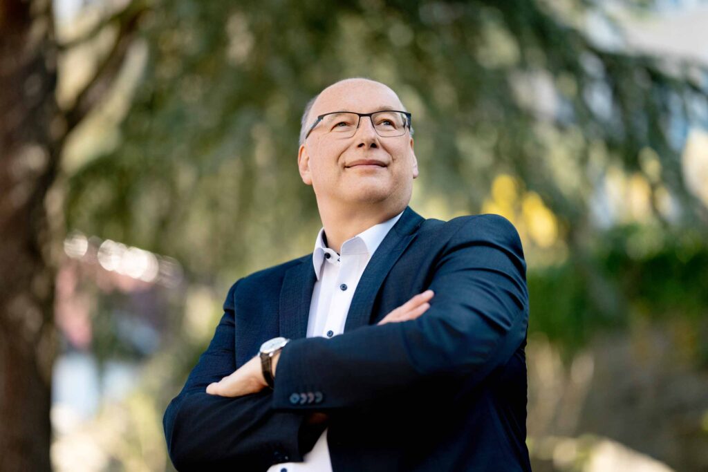 Guido steht mit verschränkten Armen vor einem Baum